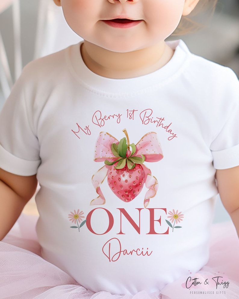 May include: White short-sleeved t-shirt with a strawberry design and the text "My Berry 1st Birthday". The design includes a pink bow, the word "ONE", and the name "Darcii". The shirt is for a baby.