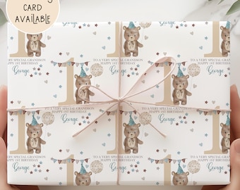 May include: White wrapping paper with a repeating pattern of teddy bears, balloons, and the number 1. The text "To a very special grandson, Happy 1st Birthday, George" is also printed on the paper. A matching card is available.