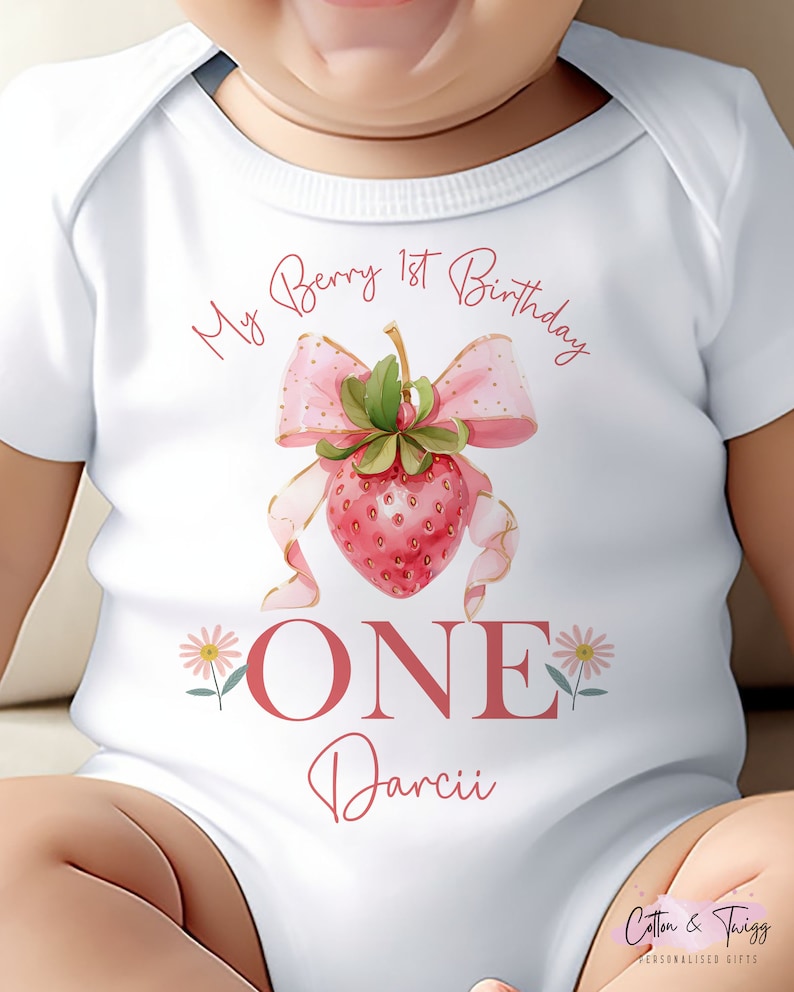 May include: White baby bodysuit with a strawberry design and the text "My Berry 1st Birthday". The design includes a pink bow, a strawberry, and the word "ONE". The name "Darcii" is also printed on the bodysuit.