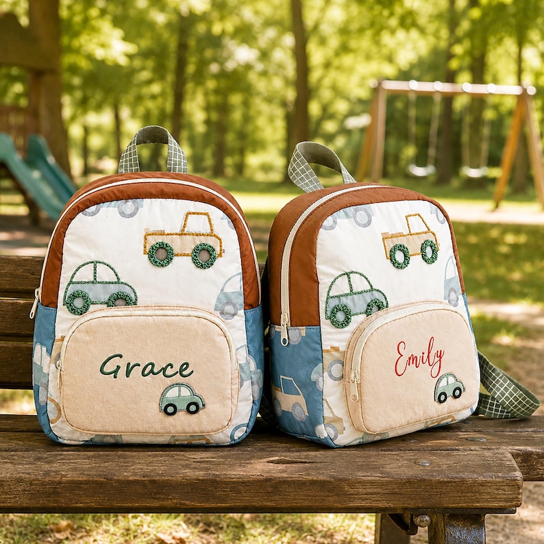 May include: Two quilted backpacks featuring a white base with a pattern of green and tan cars. Each bag has a tan front pocket with a name embroidered in green or red, and a small car appliqu&eacute;. The backpacks have brown trim and green handles.