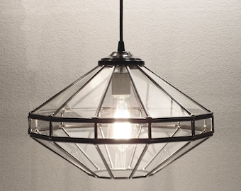 May include: A clear glass pendant light fixture with a black metal frame. The light fixture has a geometric design with multiple panes of glass.