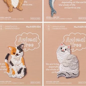 May include: Four embroidered patches featuring animals. A raccoon, a dolphin, a calico cat, and a gray cat are depicted. Each patch has the words "Animal Tree" and a short inspirational quote. The patches are on a light brown background.