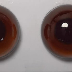 Puede incluir: Dos ojos de muñeca redondos y brillantes de color marrón, con una pupila oscura y un iris marrón claro. Los ojos tienen una superficie reflectante y están sobre un fondo blanco. Adecuado para la fabricación de muñecas y manualidades.