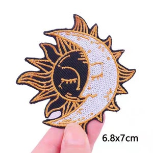 May include: Gold embroidered iron-on patch featuring a sun and moon design with closed eyes. The patch measures 6.8 by 7 centimetres.