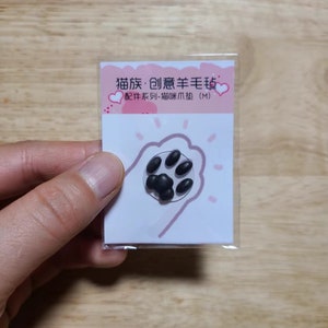 May include: A small, clear plastic package containing a black cat paw-shaped felt pad. The pad has six black oval shapes arranged to resemble a paw print. The package has text in Chinese characters and a pink border.