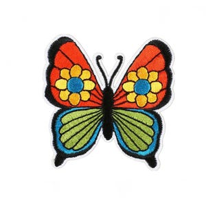 Può includere: Toppa a farfalla ricamata con un design colorato. La farfalla presenta ali arancioni e gialle con accenti blu e verdi. La toppa ha un contorno nero e si trova su uno sfondo bianco.