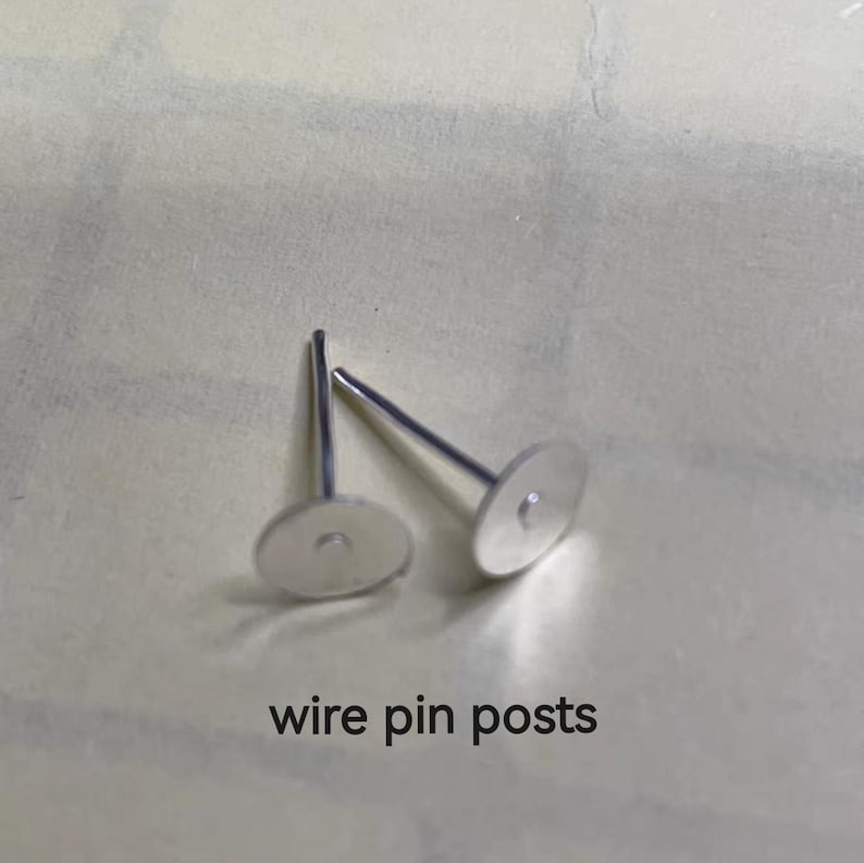 May include: Two silver wire pin posts for jewelry making. The posts have a flat, round base and a thin, straight wire.