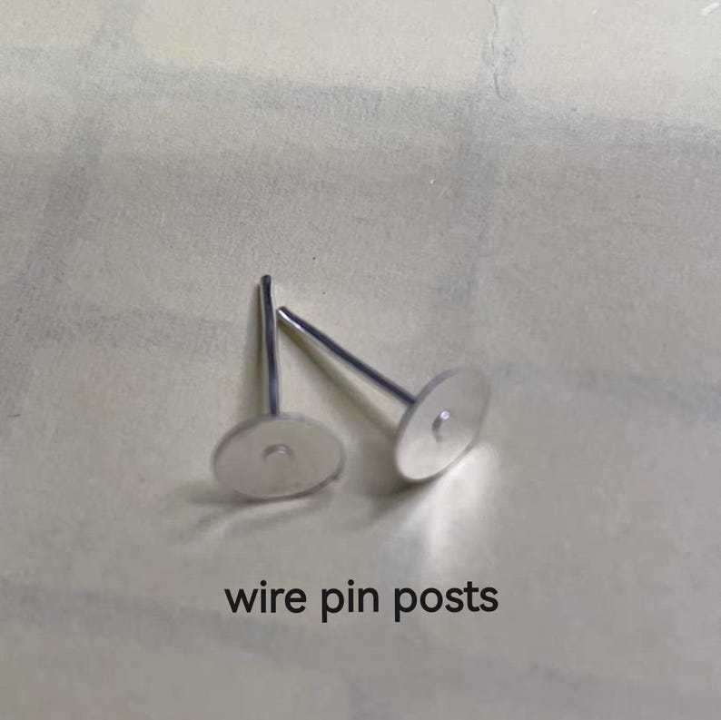 May include: Two silver-colored wire pin posts with flat, round disc tops. The posts are on a light-colored surface. The text "wire pin posts" is printed in black below the posts.