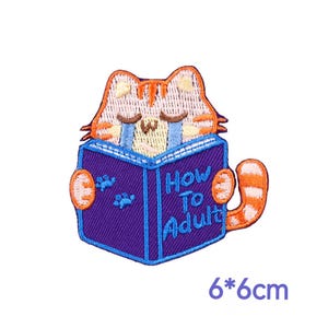 May include: Embroidered patch featuring a cartoon cat reading a book titled "How To Adult." The cat is orange and white, with blue tears. The book is purple with blue text. The patch measures 6 x 6 cm.