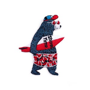 Può includere: Toppa ricamata raffigurante un orso blu con berretto rosso e blu e occhiali da sole, che tiene una tavola da surf rossa e bianca con la scritta "Show Time". L'orso indossa un costume da bagno floreale rosso e bianco.