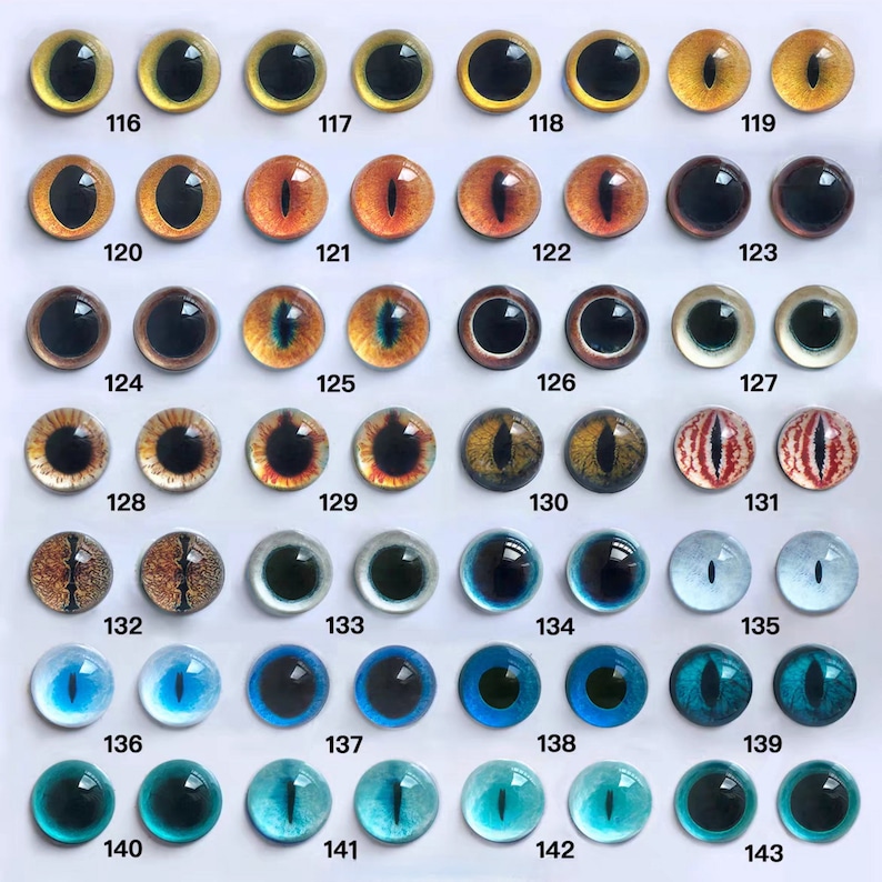 May include: A collection of glass eye cabochons in various colors and designs. The eyes range from yellow and gold to orange, brown, and blue, with black pupils. Each eye is numbered, with the numbers 116 through 143 visible.