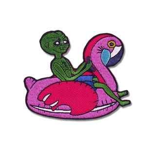 Peut inclure: Écusson brodé représentant un extraterrestre vert portant des lunettes de soleil, se relaxant sur une bouée gonflable flamant rose. L'extraterrestre porte un short bleu. Le flamant rose est rose, avec un œil blanc et bleu et un bec noir.