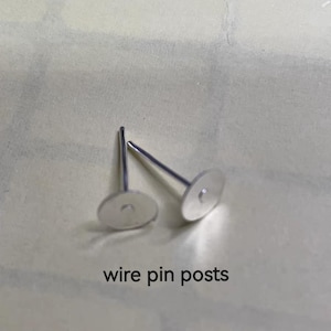 Op de afbeelding: Twee zilveren draadpinnen voor het maken van sieraden. De pinnen hebben een platte, ronde basis en een dunne, rechte draad.