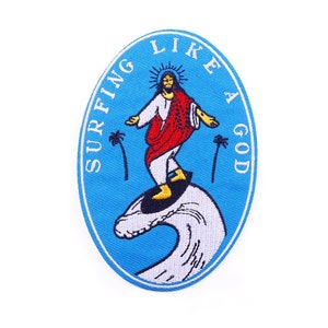 Puede incluir: Parche bordado con un borde ovalado azul con el texto "SURFING LIKE A GOD". El parche representa una figura con túnicas blancas y rojas surfeando sobre una ola, con palmeras a ambos lados.
