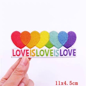 Pode incluir: Remendo bordado com seis corações coloridos do arco-íris e o texto "LOVE IS LOVE IS LOVE". O remendo mede 4,5 cm x 11 cm.