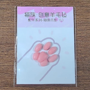 May include: A package featuring a pink paw print design with pink, oval-shaped cat paw pads. The package has Chinese text at the top and the words "Cat Paw Pads (L)" at the bottom.