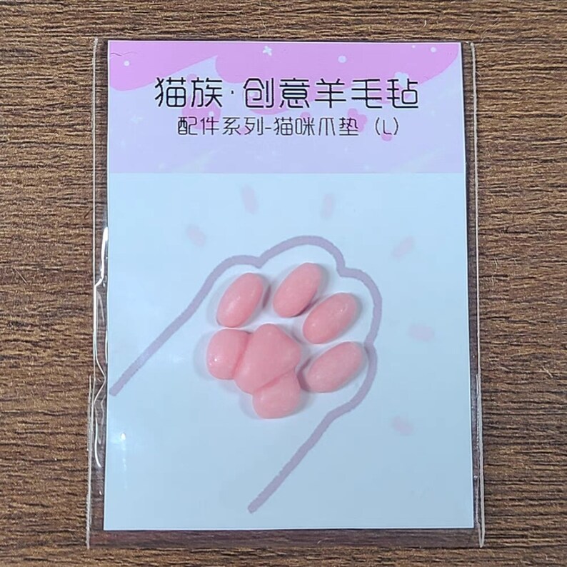 May include: A package featuring a pink paw print design with pink, oval-shaped cat paw pads. The package has Chinese text at the top and the words "Cat Paw Pads (L)" at the bottom.