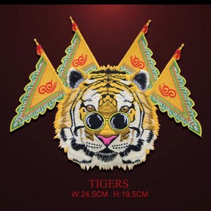 Pode incluir: Patch bordado com um tigre usando óculos redondos e bandeiras amarelas. O tigre tem um padrão listrado amarelo e preto, um nariz rosa e bigodes brancos. As bandeiras têm detalhes em vermelho e verde. O texto "TIGERS" está na parte inferior, com dimensões de L: 24,5 cm A: 19,5 cm.