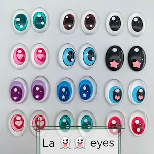 Może przedstawiać: Kolekcja owalnych oczu dla lalek w różnych kolorach, w tym zielonym, brązowym, niebieskim, różowym, fioletowym i czarnym. Niektóre oczy mają wzory serc i gwiazd. Tekst "La eyes" znajduje się na dole.