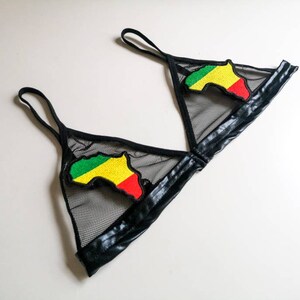 May include: Black mesh bralette with black faux leather trim and straps. The bralette features two embroidered patches of the African continent in green, yellow, and red. This lingerie item is designed for wear.