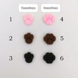 Peut inclure: Six décorations en forme de pattes de chat, roses, marron et noires. Les tailles sont de 7mm x 9mm et 9mm x 9mm. Idéal pour les loisirs créatifs ou la fabrication de bijoux. Le texte indique les dimensions.