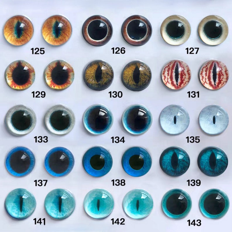 May include: A collection of glass eye cabochons in various colors and designs. The eyes include shades of brown, yellow, red, blue, and green, with different pupil shapes. Each eye is numbered, ranging from 125 to 143.