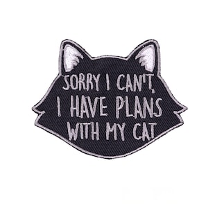 Op de afbeelding: Een zwarte katvormige patch met witte geborduurde tekst: "SORRY I CAN'T, I HAVE PLANS WITH MY CAT." De patch heeft een witte rand en witte accenten op de oren van de kat.