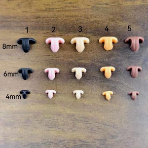 Può includere: Una collezione di piccoli nasi artigianali in plastica a forma di T, in vari colori, tra cui nero, rosa, beige, arancione e marrone. Le dimensioni variano da 4 mm a 8 mm. I nasi sono disposti su una superficie di legno.