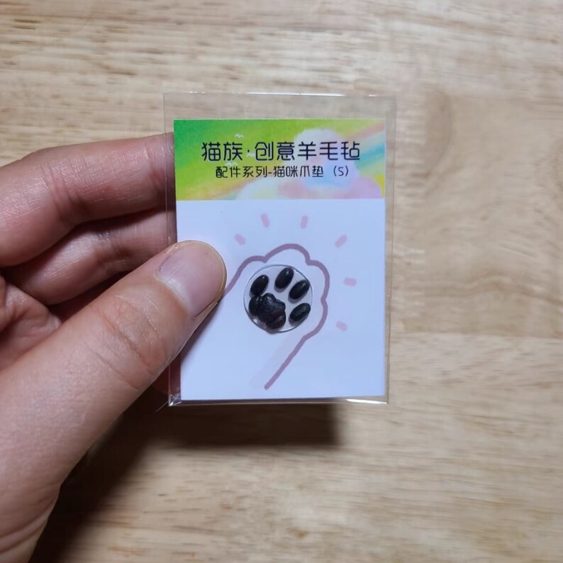 May include: A small, clear sticker featuring a black cat paw print design. The sticker is on a white background with a pink outline of a hand. Text in Chinese characters is visible at the top.