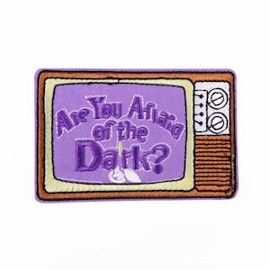 May include: Embroidered patch featuring a retro television design. The screen is purple with the text "Are You Afraid of the Dark?" in white and purple. The TV has a yellow border, and a brown frame.