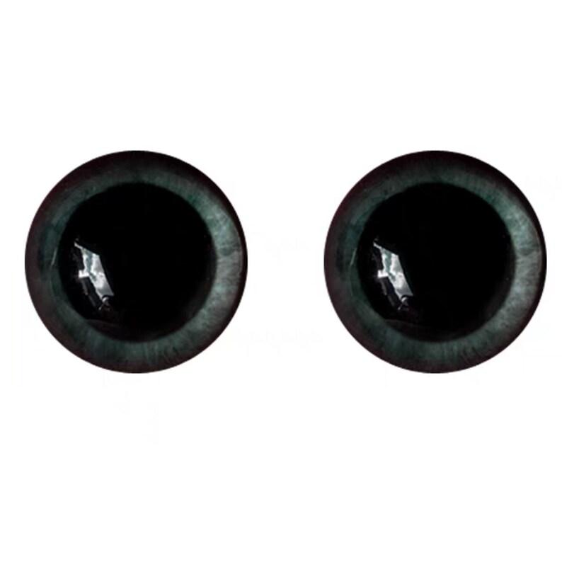 Puede incluir: Dos ojos redondos de color verde azulado oscuro con pupilas negras. Los ojos tienen una cualidad reflectante, lo que sugiere un acabado brillante. Los iris son de un verde azulado apagado y las pupilas son de un negro profundo, creando un contraste llamativo.