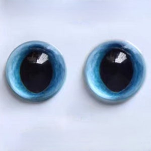 May include: Two round glass eyes with a light blue iris and a black pupil. The eyes have a reflective surface, set against a white background. These craft supplies are ideal for doll making or other artistic projects.