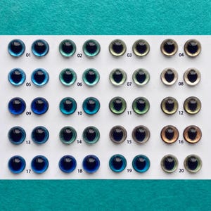 Op de afbeelding: Een vel met 20 paar plastic poppenogen in verschillende kleuren, waaronder blauw, groen, bruin en grijs. De ogen zijn genummerd van 01 tot en met 20.