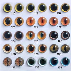 May include: A collection of glass eye cabochons in various colors and designs. The eyes have black pupils and range in color from yellow to orange, brown, and blue. Each eye is numbered, with the numbers 116 through 134 visible.