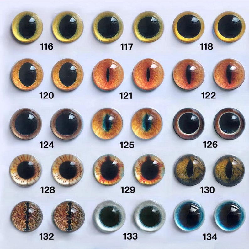 May include: A collection of glass eye cabochons in various colors and designs. The eyes have black pupils and range in color from yellow to orange, brown, and blue. Each eye is numbered, with the numbers 116 through 134 visible.