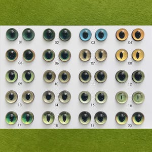 May include: A collection of twenty glass eye cabochons in various colors and designs. The eyes range from green, blue, and brown, with different pupil shapes. Each eye is numbered from 01 to 20.