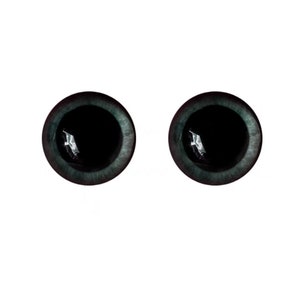 Puede incluir: Dos ojos redondos de artesan&iacute;a, de color verde azulado oscuro, con pupilas negras. Los ojos tienen una cualidad reflectante, lo que sugiere un material de vidrio o resina. Los iris tienen una apariencia sutil y texturizada, y el fondo es blanco liso.