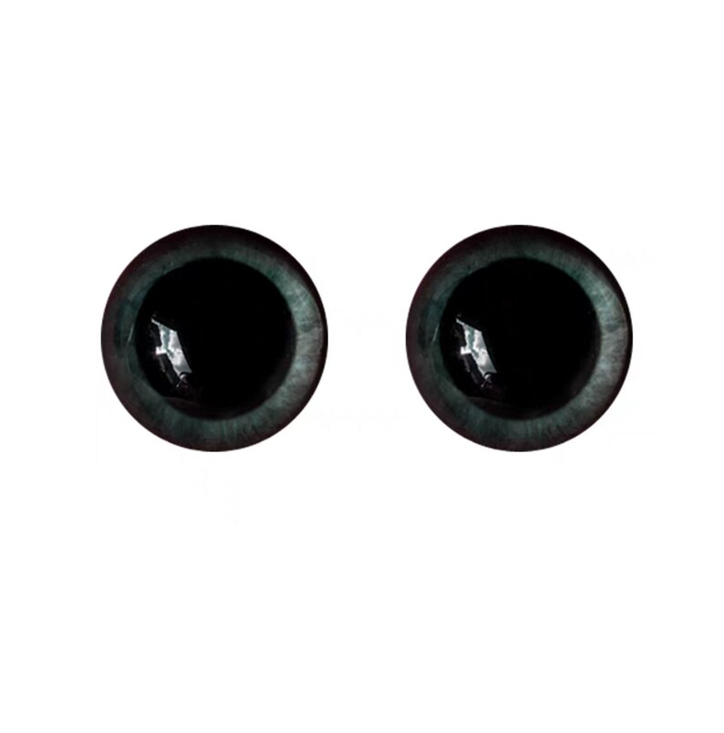 Puede incluir: Dos ojos redondos de artesan&iacute;a, de color verde azulado oscuro, con pupilas negras. Los ojos tienen una cualidad reflectante, lo que sugiere un material de vidrio o resina. Los iris tienen una apariencia sutil y texturizada, y el fondo es blanco liso.