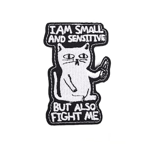Può includere: Toppa ricamata con un gatto bianco che tiene un coltello. Il testo "I AM SMALL AND SENSITIVE" è sopra il gatto, e "BUT ALSO FIGHT ME" sotto. Il gatto ha un'espressione seria. Toppa in bianco e nero.