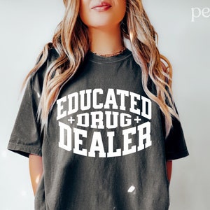 Op de afbeelding: Een donkergrijs T-shirt met witte tekst die "Educated + Drug + Dealer" luidt.