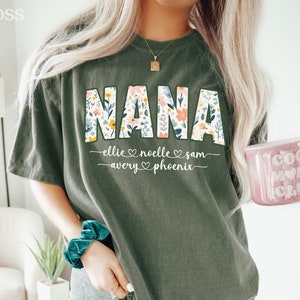 K&ouml;nnte beinhalten: Ein gr&uuml;nes T-Shirt mit dem Wort "NANA" in Blumenbuchstaben. Das Shirt tr&auml;gt die Namen "Ellie, Noelle, Sam, Avery, Phoenix" unter dem Wort "NANA".