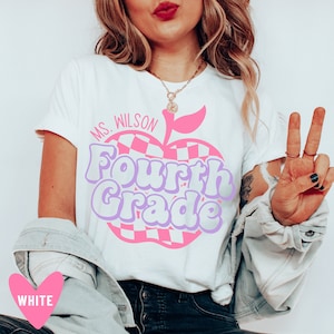 K&ouml;nnte beinhalten: Wei&szlig;es T-Shirt mit einem pinkfarbenen und violetten Apfel-Motiv, auf dem "Ms. Wilson Fourth Grade" steht.