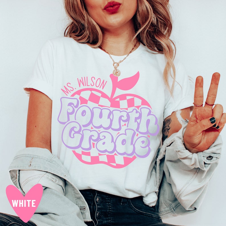 K&ouml;nnte beinhalten: Wei&szlig;es T-Shirt mit einem pinkfarbenen und violetten Apfel-Motiv, auf dem "Ms. Wilson Fourth Grade" steht.