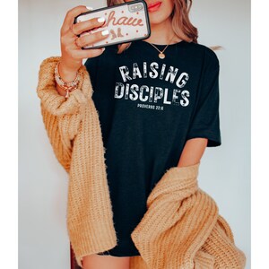 May include: Black t-shirt with white text that reads "Raising Disciples Proverbs 22:6".