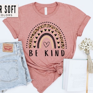 May include: A pink t-shirt with a rainbow design featuring leopard print and black hearts. The text "BE KIND" is printed below the rainbow.