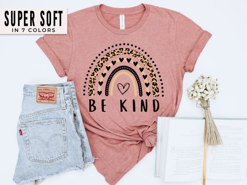 May include: A pink t-shirt with a rainbow design featuring leopard print and black hearts. The text "BE KIND" is printed below the rainbow.