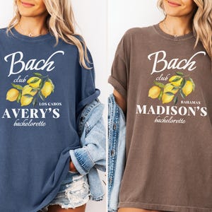 May include: Two t-shirts, one denim blue and one espresso brown, each with a white graphic. The graphic includes the words "Bach club" above a lemon branch illustration and the name "Avery's" or "Madison's" with "bachelorette" below.