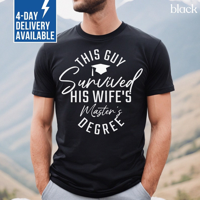 Peut inclure: T-shirt noir avec un texte blanc qui dit "This Guy Survived His Wife's Master's Degree". Le texte est dans un cercle avec une ic&ocirc;ne de chapeau de graduation au-dessus du mot "Survived".
