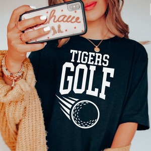 May include: Black t-shirt with white text that reads "TIGERS GOLF" and a white golf ball graphic.