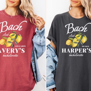 May include: Crimson and pepper-colored t-shirts with white text and a lemon illustration. The shirts read "Bach Club" with a bachelorette party location and name. The crimson shirt says "Los Cabos, Avery's bachelorette". The pepper shirt says "Mexico, Harper's bachelorette".